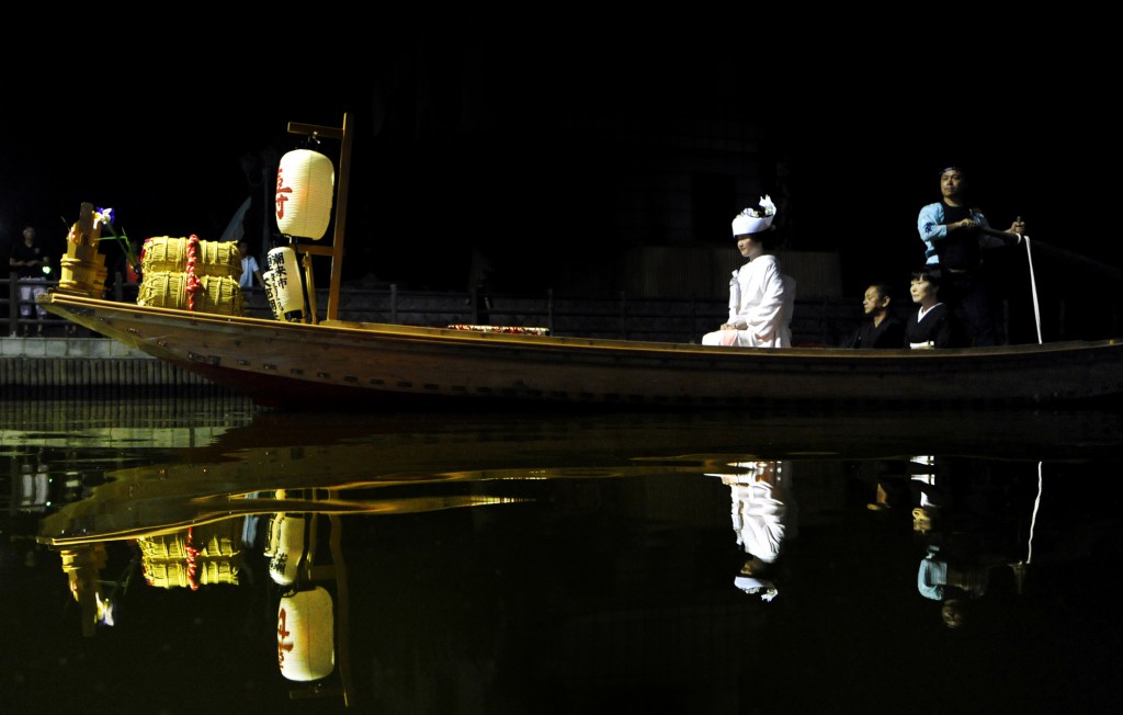 Bridal boat traveling on water with bride dressed in white shiromuku kimono. Sound of oar echoes in the darkness.  