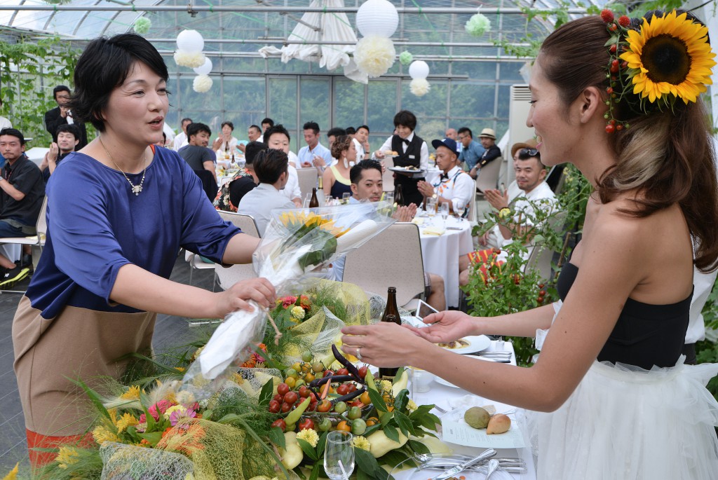Michiyo Koyama (left) handing over flower bouquet for bouquet toss to bride (right). Koyama decorated venue with flowers and vegetables she sowed and grew.  