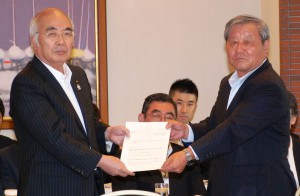 A photo taken on Friday, Aug. 8, provided by the Central Union of Agricultural Co-operatives (JA-Zenchu), shows JA-Zenchu President Akira Banzai (left) handing a letter to Kazuo Kimura, head of an advisory council, requesting the council to discuss reform of the JA group.　(Courtesy of JA-Zenchu)