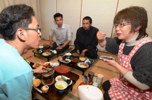 Fumiko Yanada explaining how to eat Sukiyaki with gestures and using translation app on smart phone.