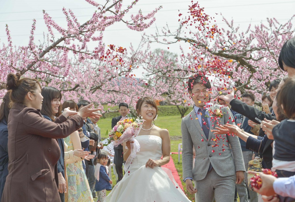 Guests celebrating Jumpei and Akina with flower shower while they walk down open aisle (in Fuefuki-shi, Yamanashi Prefecture)